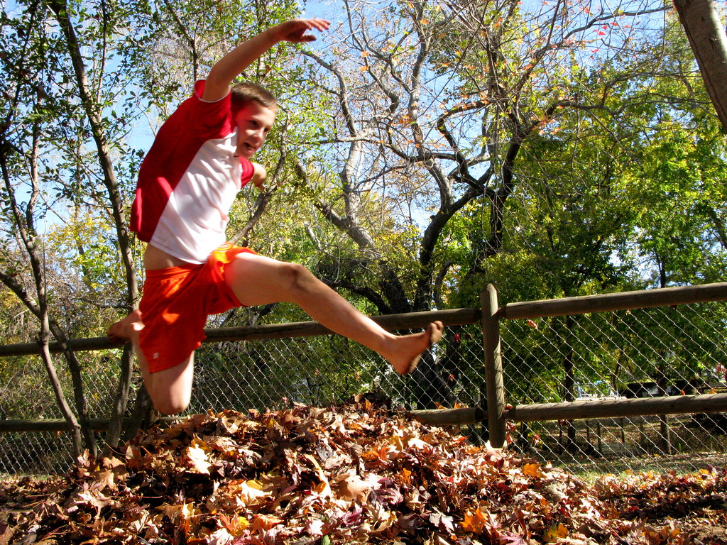 A boy jumping over a pile of leaves
