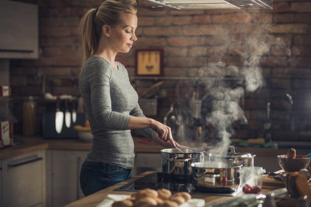 Young woman standing in the kitchen and cooking soup for lunch.