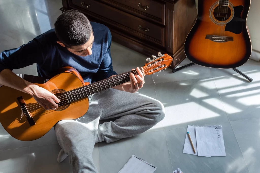 There is a guy sitting on the floor playing and writing music