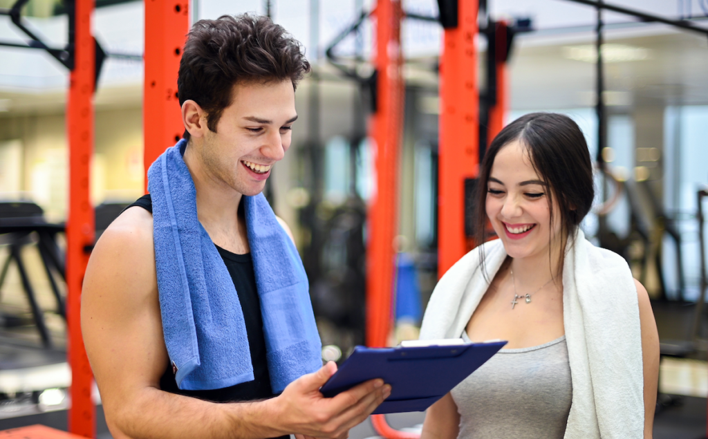 Call Center English, talking about Healthy Lifestyle Choices two young adults having a conversation in a gym looking at board as if going over a routine